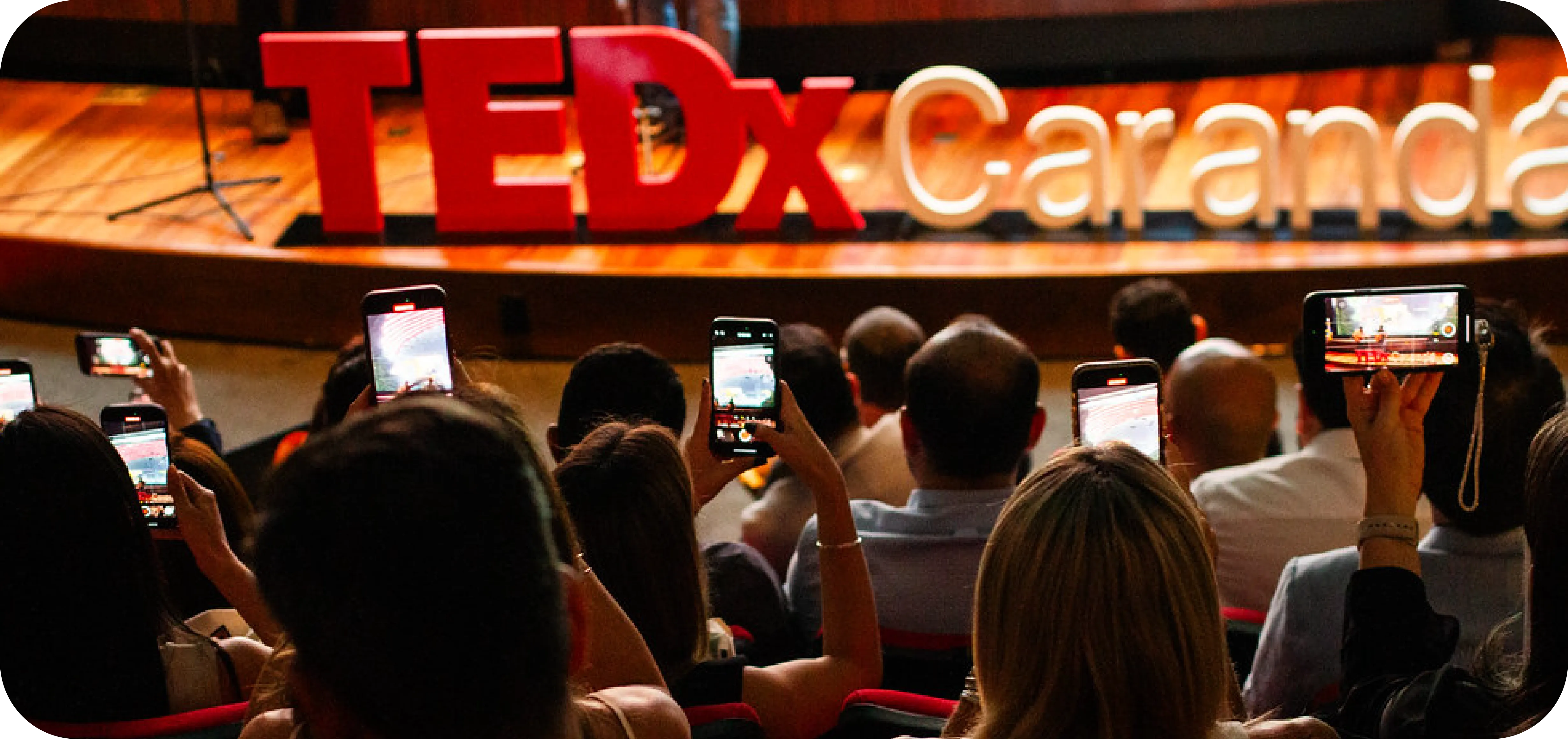 Plateia filma o palco com letreiro TEDxCarandá